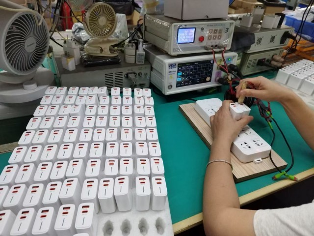 Worker testing a white power adapter using instruments at a QC station, showcasing Fita's strict quality inspection for B2B orders.